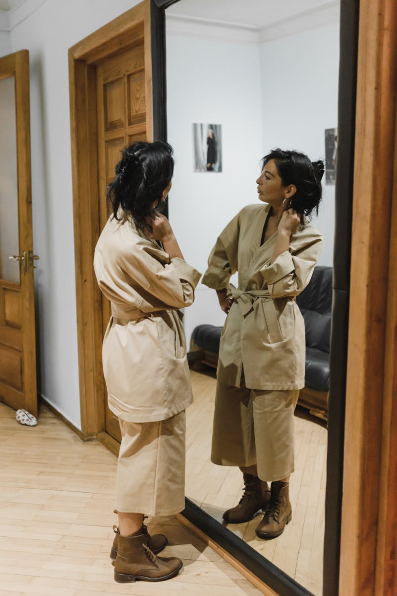 Woman in beige attire posing in front of a mirror indoors.